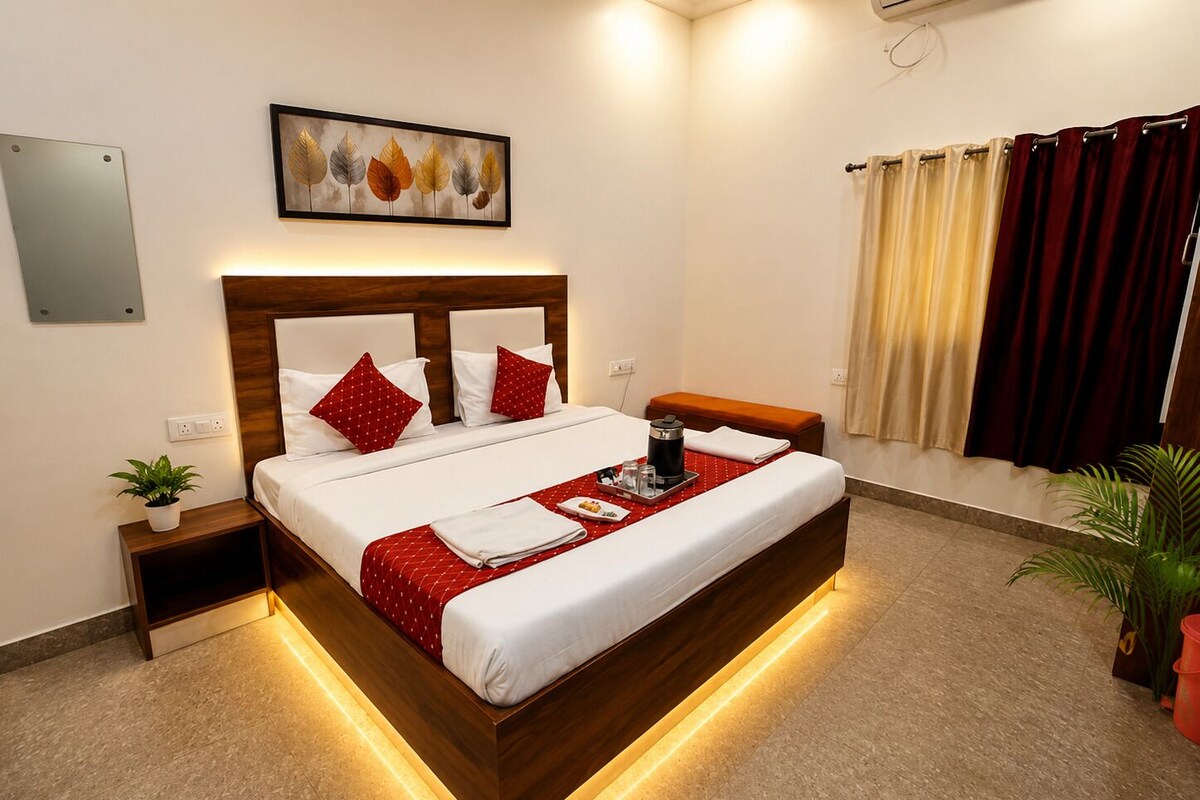 Habitación de hotel moderna con una cama grande, mesitas de noche, una planta en la mesita y un cuadro en la pared, además de un ventanal con cortinas.