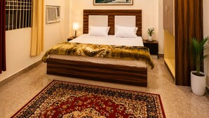 Une chambre d’hôtel avec un lit, un ventilateur de plafond, un tableau, une plante en pot et une fenêtre avec des rideaux.