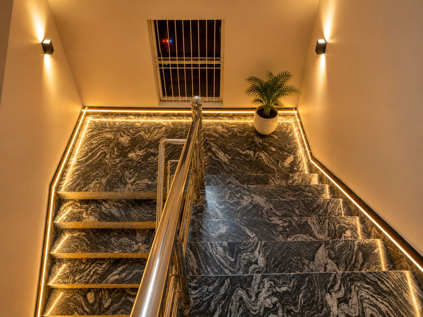 Una escalera con barandilla, escalones de mármol y una planta en maceta.