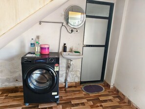 Uma área de lavanderia compacta, com máquina de lavar frontal, pia pequena e espelho.