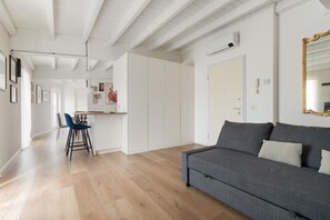Ein modernes Interieur mit einem grauen Sofa, Holzboden, weißen Wänden und einer Küchenzeile.