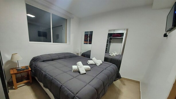 A modern bedroom with a large bed, a bedside table with a lamp, a mirror, and a TV mounted on the wall. - Taniri Fueguino: Your modern and quiet refuge at the end of the world. (Ushuaia)
