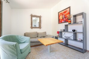 Ein Wohnzimmer mit einem grünen Sessel, einem grauen Sofa, einem Holztisch, einem Spiegel, einem Gemälde und einer grauen Regaleinheit mit verschiedenen Gegenständen.