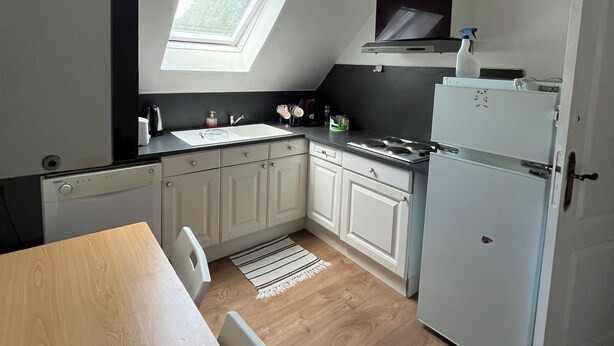 A compact kitchen with white cabinets, a wooden dining table, and a skylight. - Guestroom (Savigny-le-Temple)