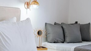 A neatly made bed with white and gray bedding, a bedside table with a decorative lamp, and a wall-mounted light fixture. -  Sea & You Luxury Beach House – Your Private Cycladic Escape (Kamari)