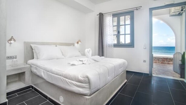 A bedroom with a bed, a window, and a view of the sea. - Sea & Sun Luxury Beach House – Elegant Cycladic Studio by Agia Paraskevi Beach (Kamari)
