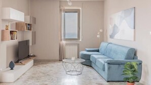 Ein modernes Wohnzimmer mit einem blauen Sofa, einem Glastisch und einem Fernseher auf einem Holzboden.