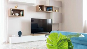 Ein modernes Wohnzimmer mit Flachbildfernseher, Einbauschränken und einem blauen Sofa.