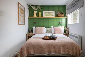 A bedroom with a green wall, a bed with patterned bedding, a bedside table with a bottle, glasses, and a tray with food.