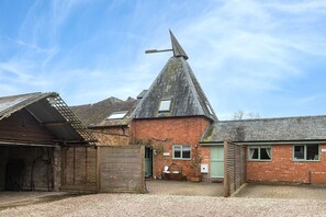 A building with a conical roof, a wooden bench, a small garden, and a gravel driveway.