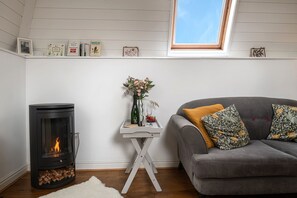 A cozy living room with a fireplace, a sofa, a small table with a vase of flowers, and a window with a view.