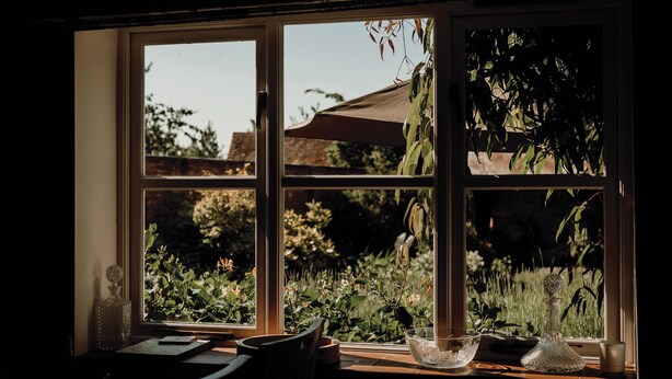 A window with a view of a garden and a table with a vase and a book.
