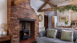 Ein gemütliches Wohnzimmer mit Kamin aus Backstein, einem grauen Sofa und einem Holzbalken an der Decke.