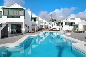 A pool area with white buildings, a clear sky, and a palm tree. - Vacation Home 'Sun Apartment' with Wi-Fi and Ventilation System (Puerto del Carmen)