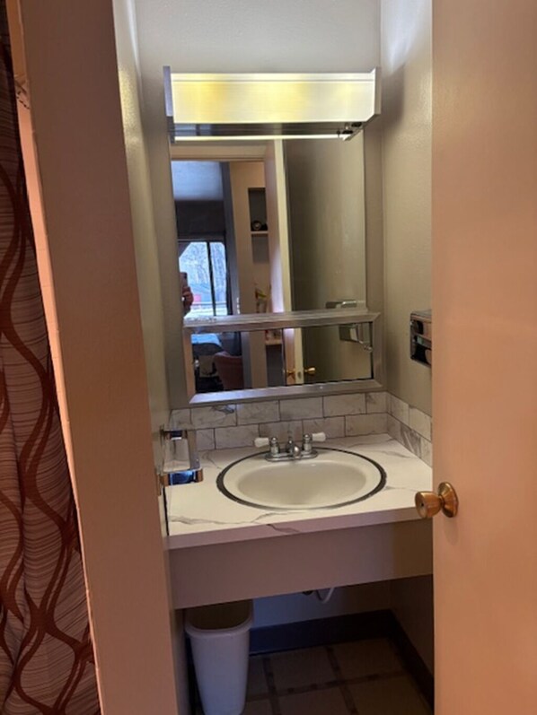 A bathroom with a white sink, a mirror, and a light above it.