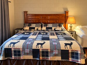 Ein Bett mit einer gesteppten Decke mit Tiermotiven, einem Holz-Kopfteil, einer Nachttischlampe und einem Nachttisch.