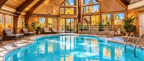 Una amplia piscina interior con arquitectura de madera, rodeada de sillones de descanso y plantas en macetas.