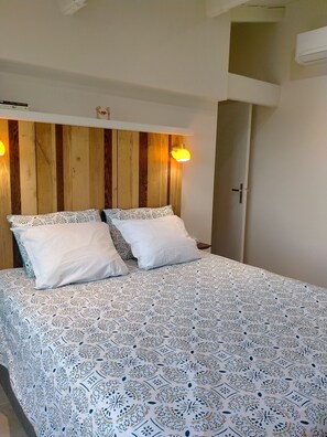 Ein Bett mit gemustertem Bettbezug, zwei weiße Kissen und ein Holz-Kopfstück mit an der Wand befestigten Lampen.