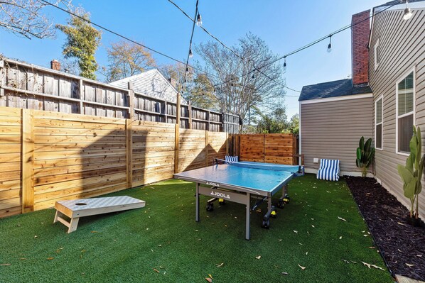 A ping pong table in a backyard with artificial grass, a wooden fence, and a house in the background. - NEW! The Green - MiniGolf+PingPong+Games+Firepit in Augusta, GA (Augusta)