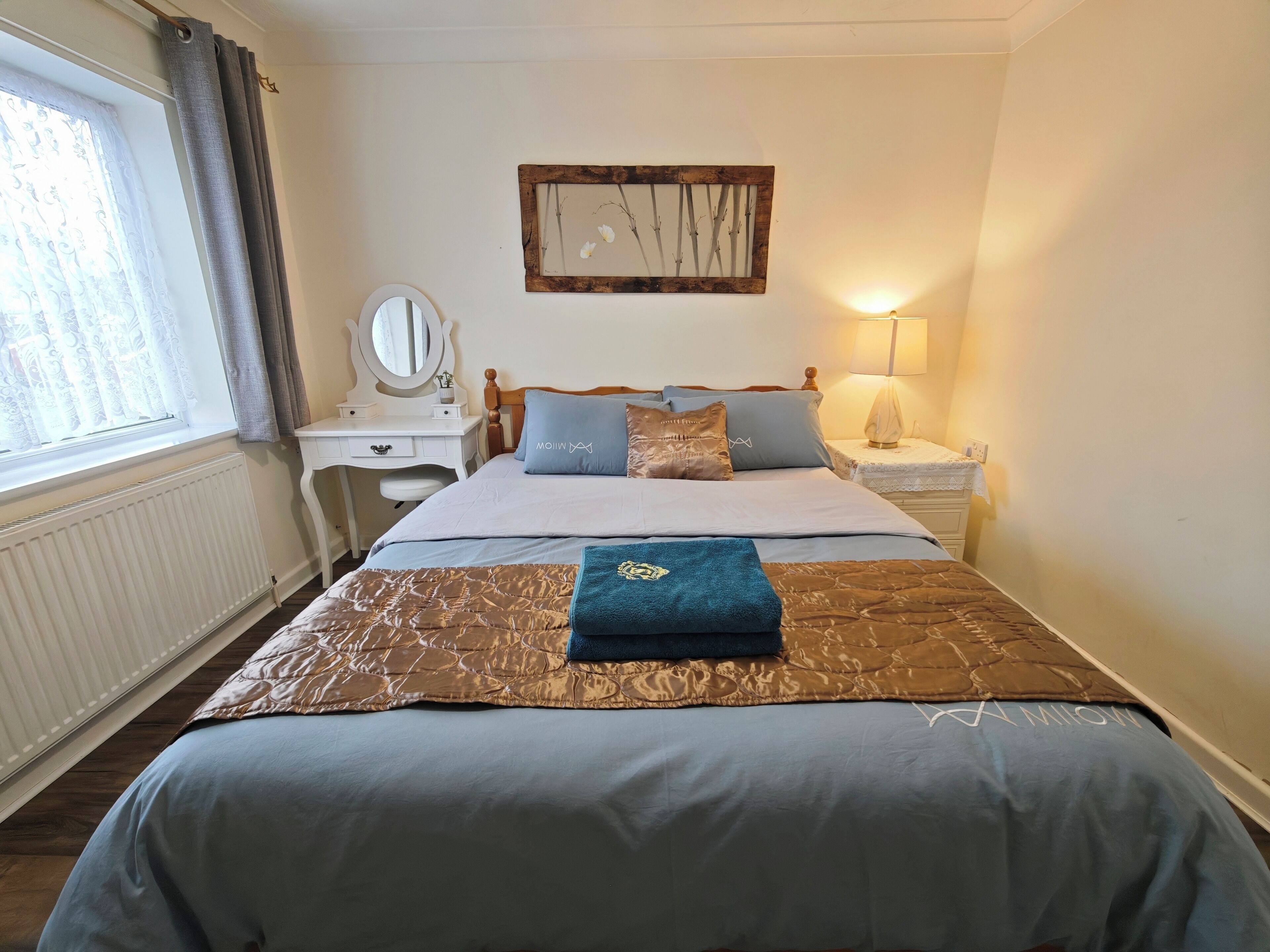 A neatly arranged bedroom with a bed, bedside tables, a mirror, and a wall-mounted artwork.