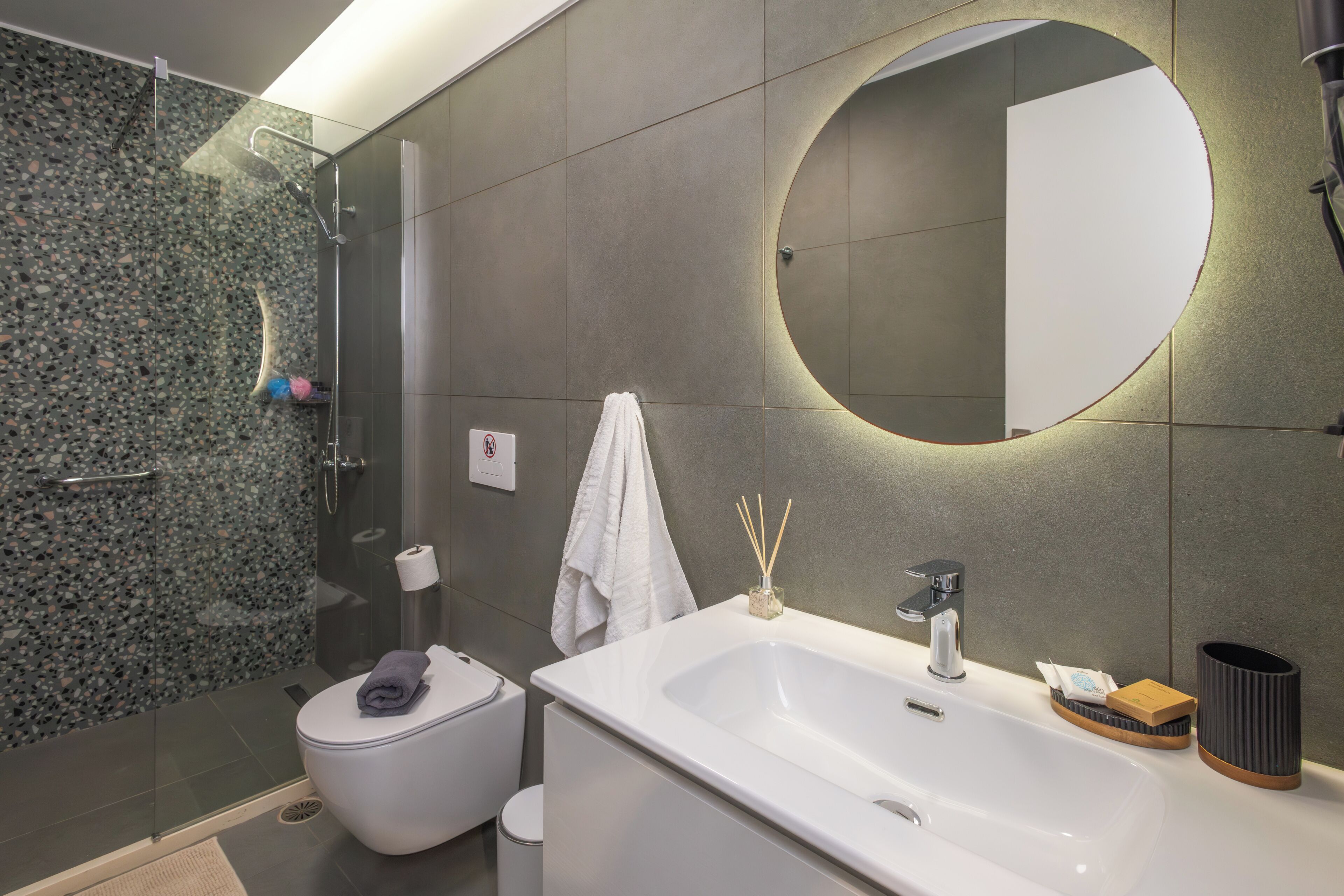 Ein modernes Badezimmer mit Duschkabine aus Glas, Toilette, Waschbecken mit Spiegel und Handtuchhalter.