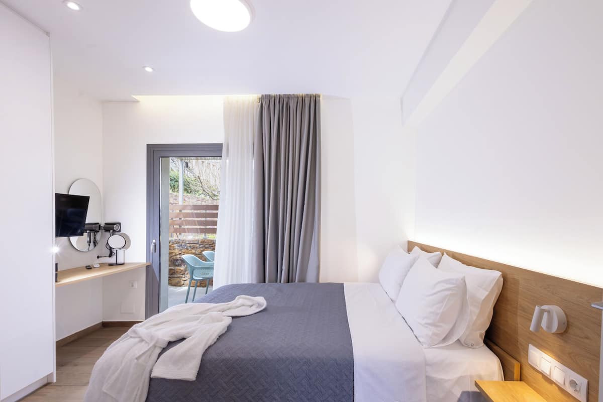A modern hotel room with a bed, bedside table, TV, and a view of the outside.