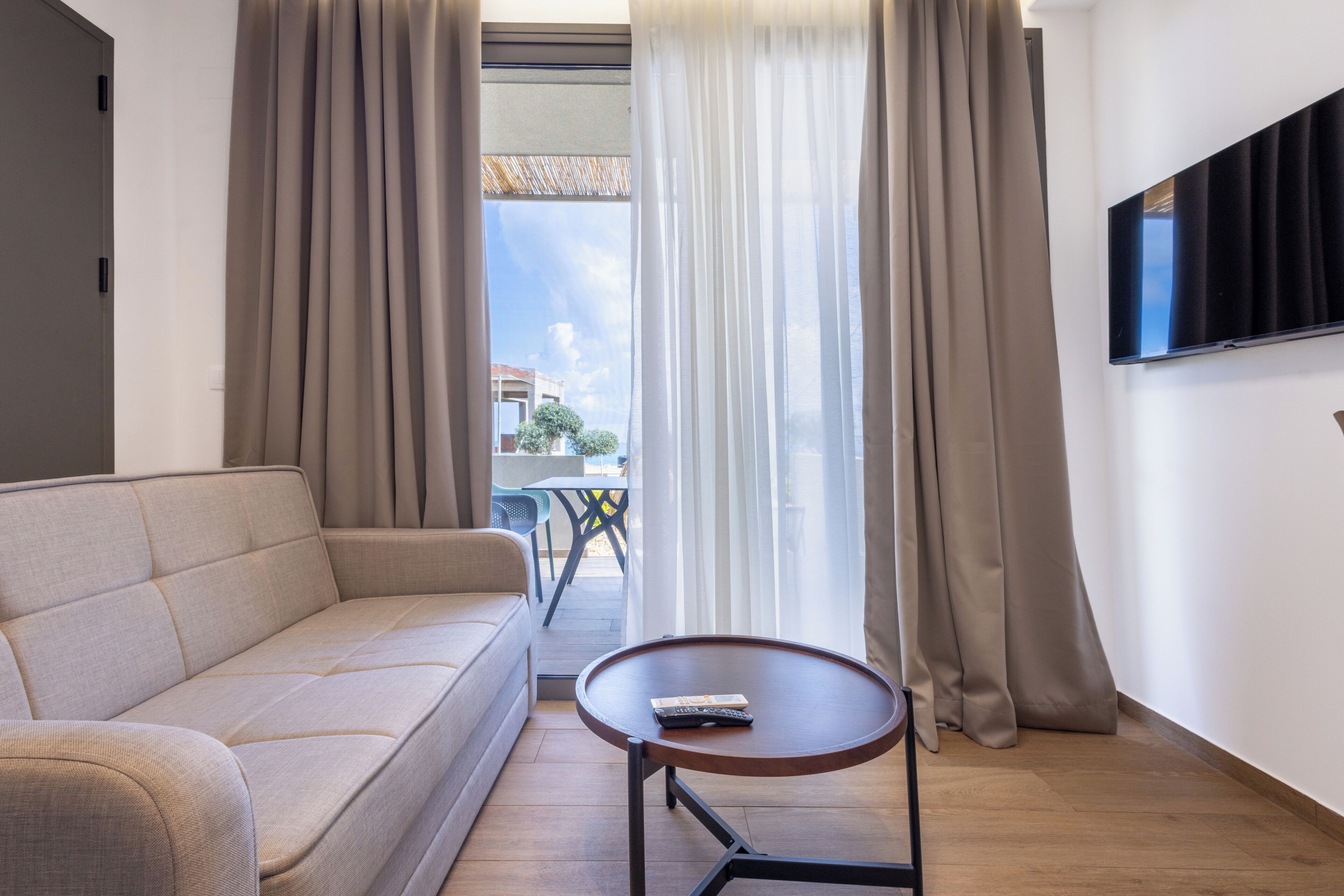En moderne stue med sofa, lille rundt bord og fjernsyn monteret på væggen.