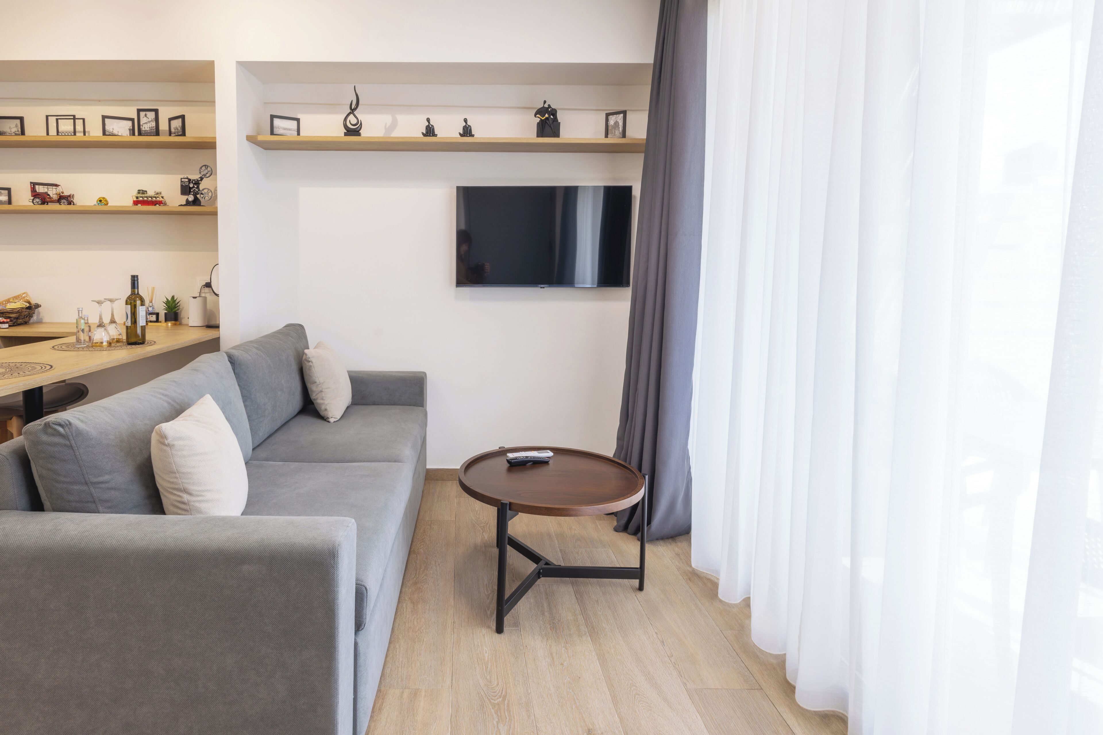 A modern living room with a grey sofa, a round coffee table, and a TV mounted on the wall.