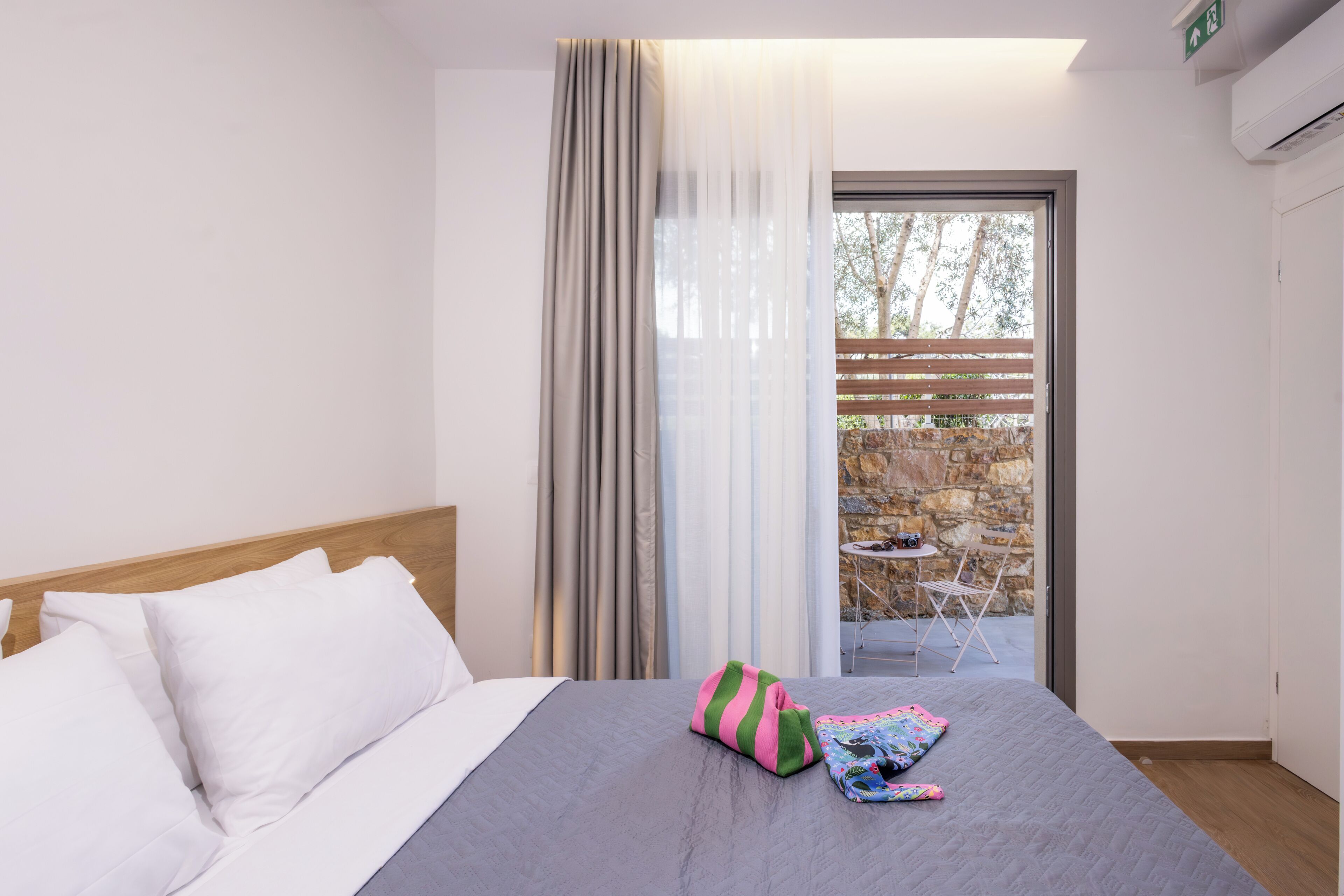 A hotel room with a bed, a window with curtains, a view of an outdoor area, and a small table with chairs.