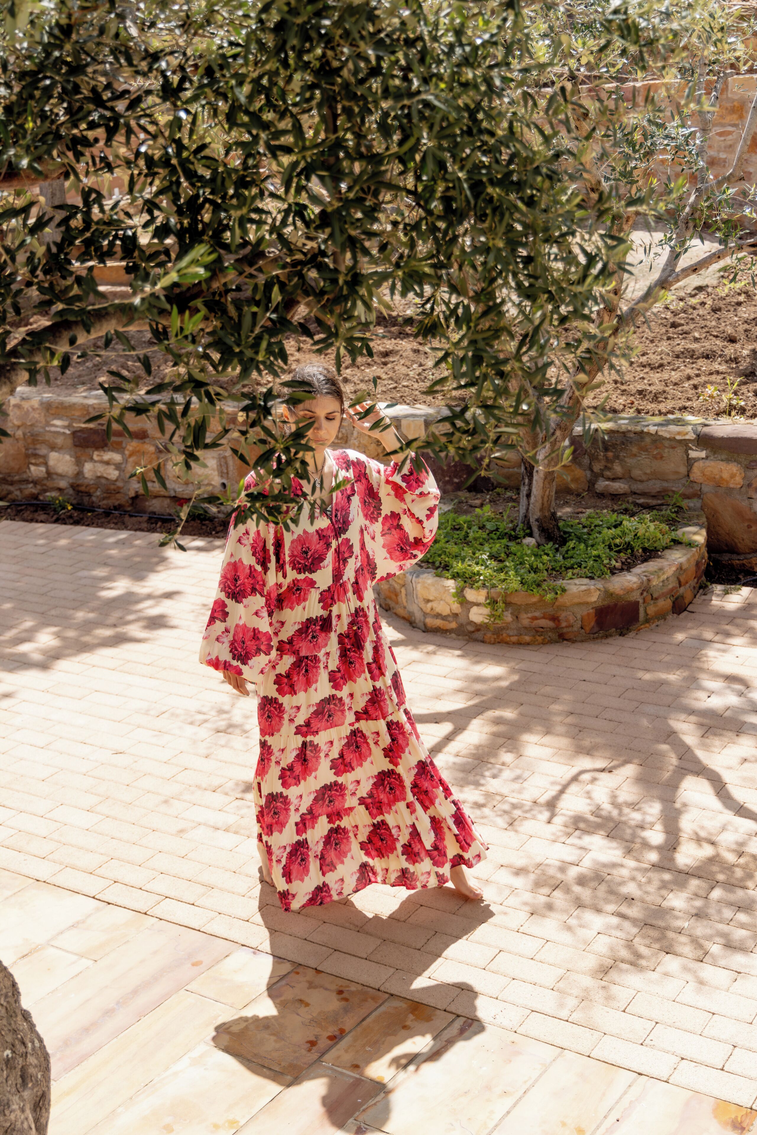 A person in a patterned dress walking on a paved area with stone walls and greenery.
