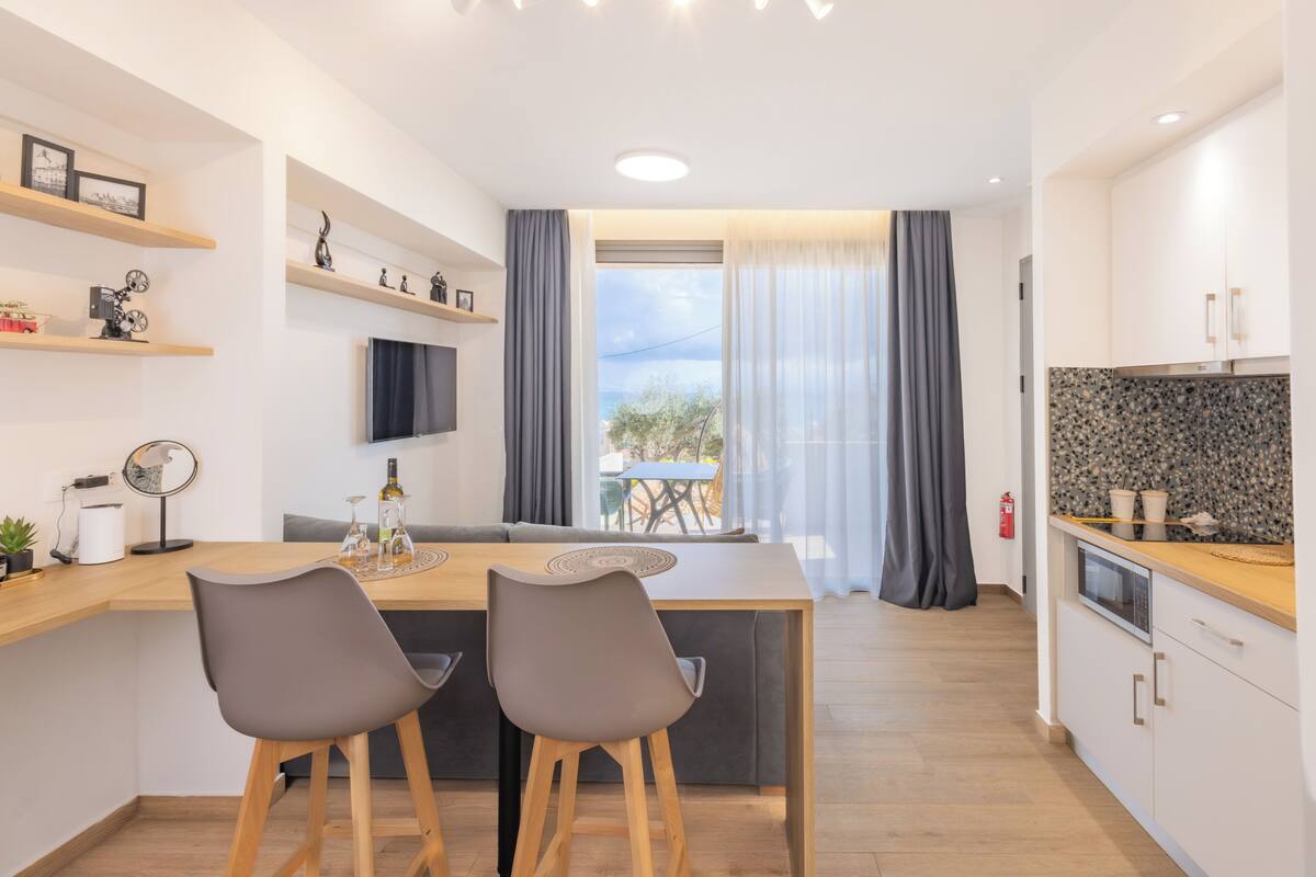 A modern kitchen with a dining area, wooden bar stools, and a view to the outside.