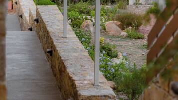 A stone pathway leading to a covered area with a metal roof, surrounded by greenery and a body of water.