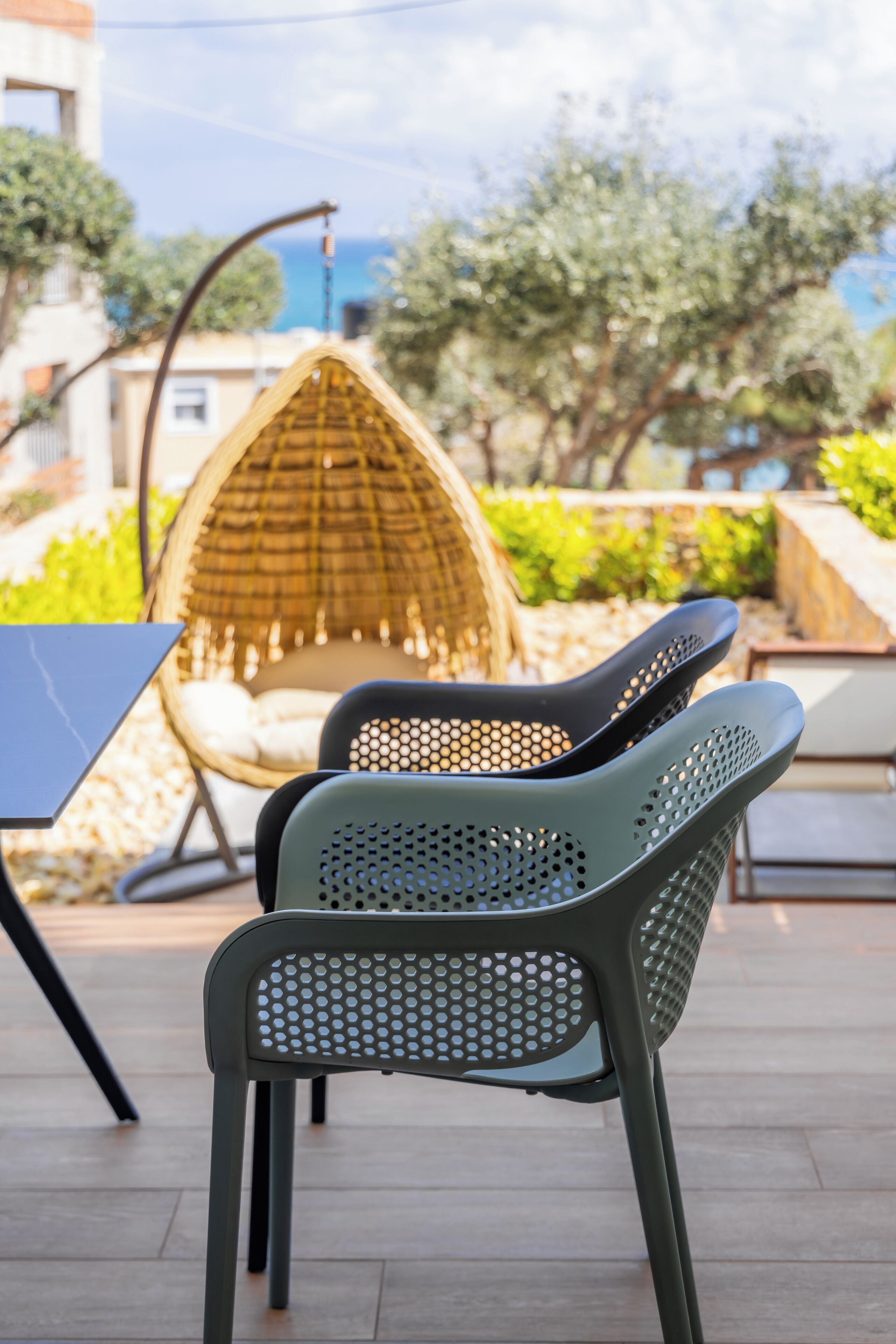 A patio with two green chairs, a wicker hanging chair, and a laptop on a table.
