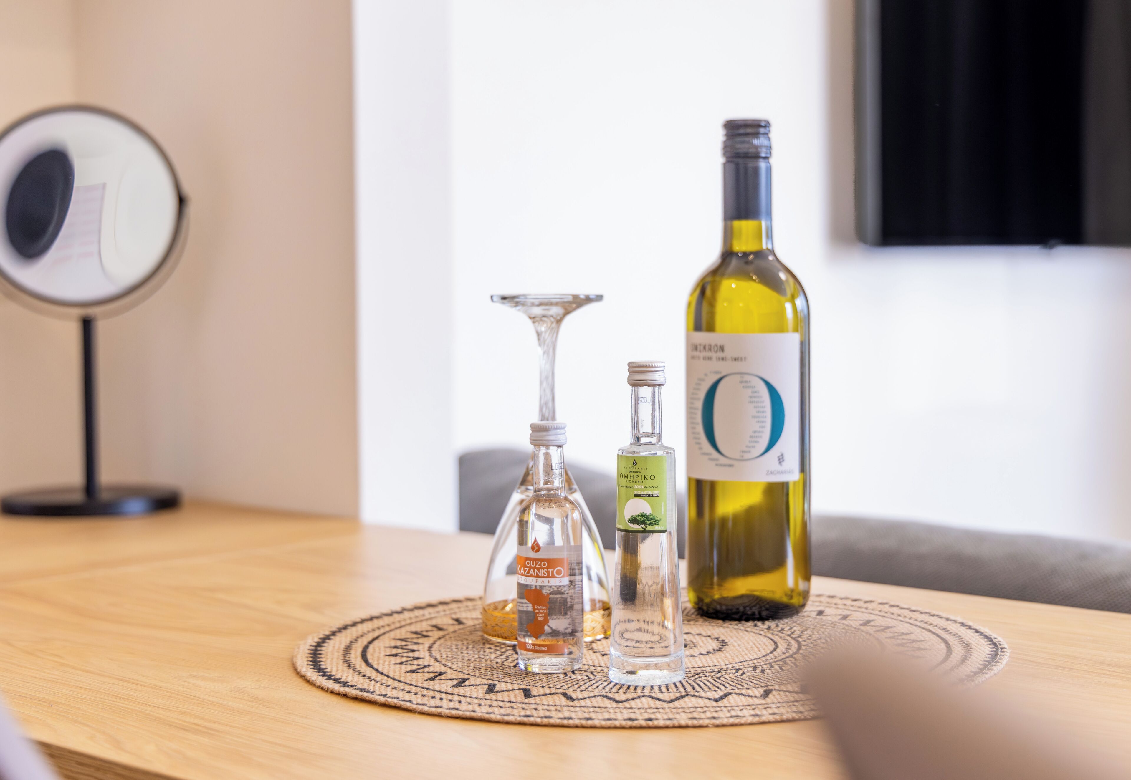 Ein Tisch mit einer Weinflasche, Olivenöl und einem Glas auf einer gewebten Tischmatte.