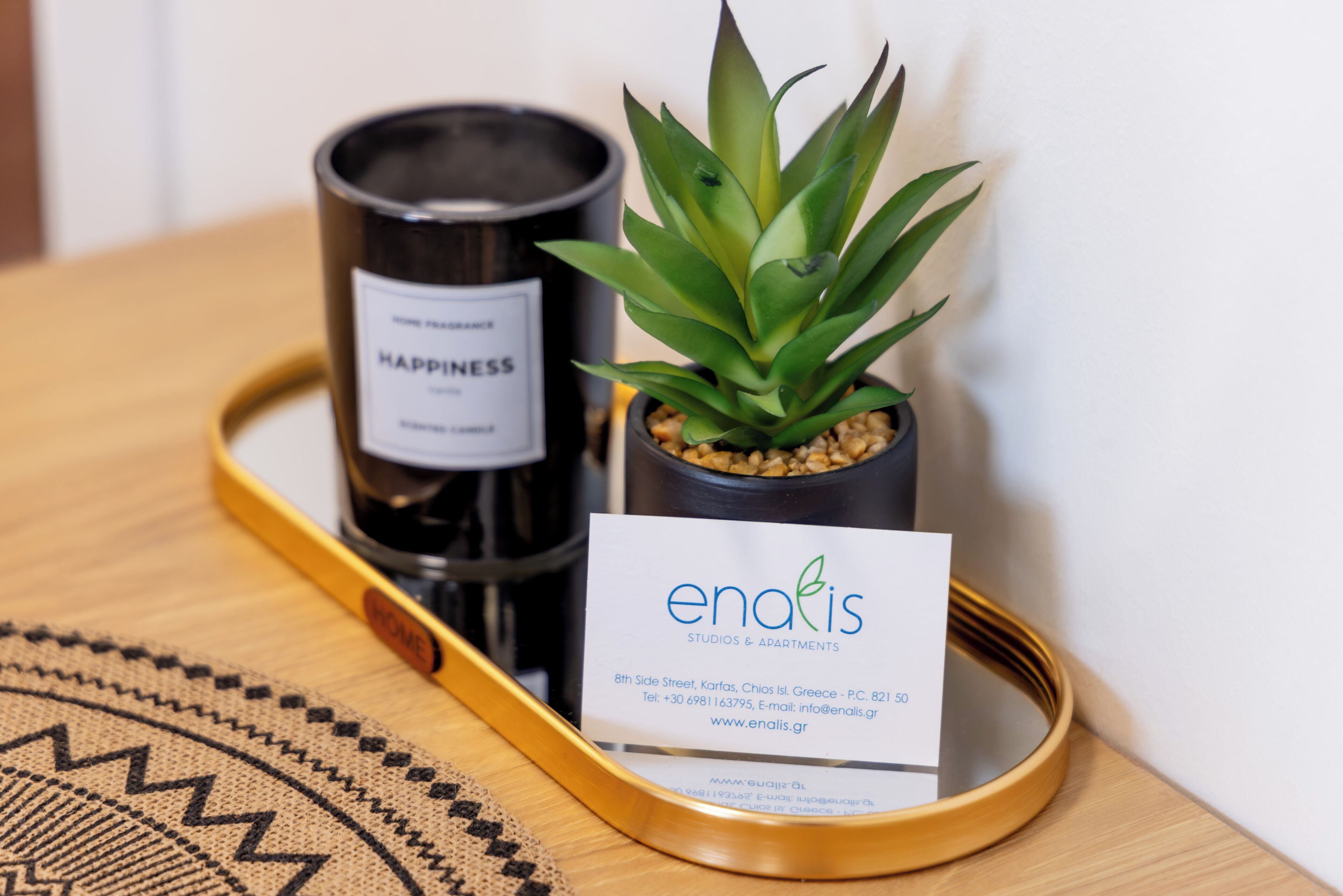 A tray with a candle labeled 'HAPPINESS,' a small potted plant, and a business card for 'enafis Studios & Apartments.'