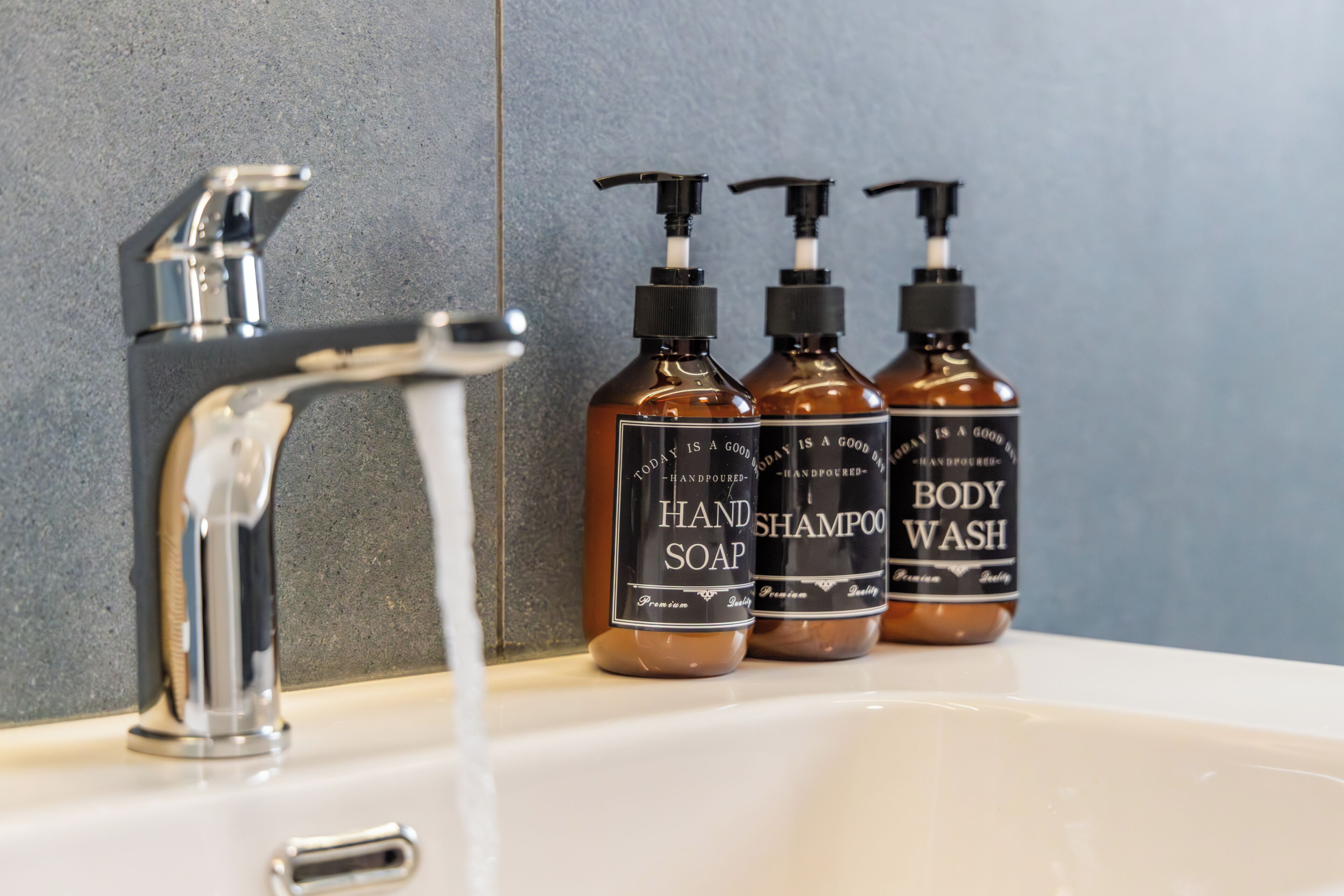 Un lavabo de salle de bain avec un robinet chromé et trois bouteilles de savon pour les mains et de gel douche.