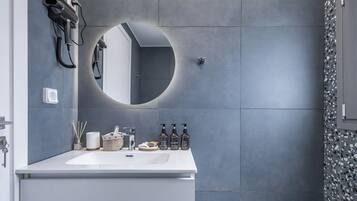 Un baño moderno con un lavamanos blanco, un espejo redondo y artículos de aseo en la encimera.