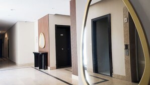 A hotel corridor with a polished marble floor, a round mirror, and two black doors. - Stylish 3BR Serviced Aprt Pool View Sodic Villette (Cairo Governorate)