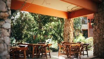 Une terrasse extérieure avec des tables et des chaises en bois, entourée de verdure et de murs en pierre.