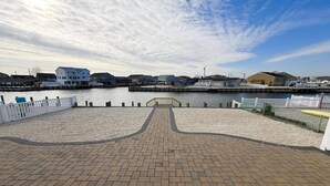 En strandpromenad med en asfalterad gångväg, ett trästaket och utsikt över byggnader på andra sidan vattnet.
