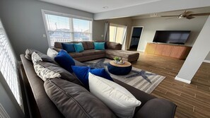 A modern living room with a sectional sofa, a round coffee table, and a flat-screen TV. - Boater & Beach Lover’s Retreat (Manahawkin)