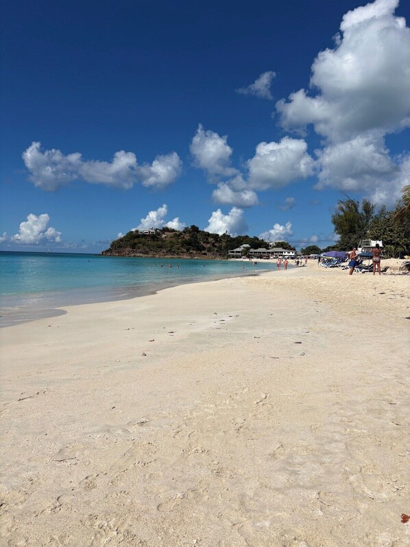 A beach with clear turquoise water, a sandy shore, and a few beach umbrellas.