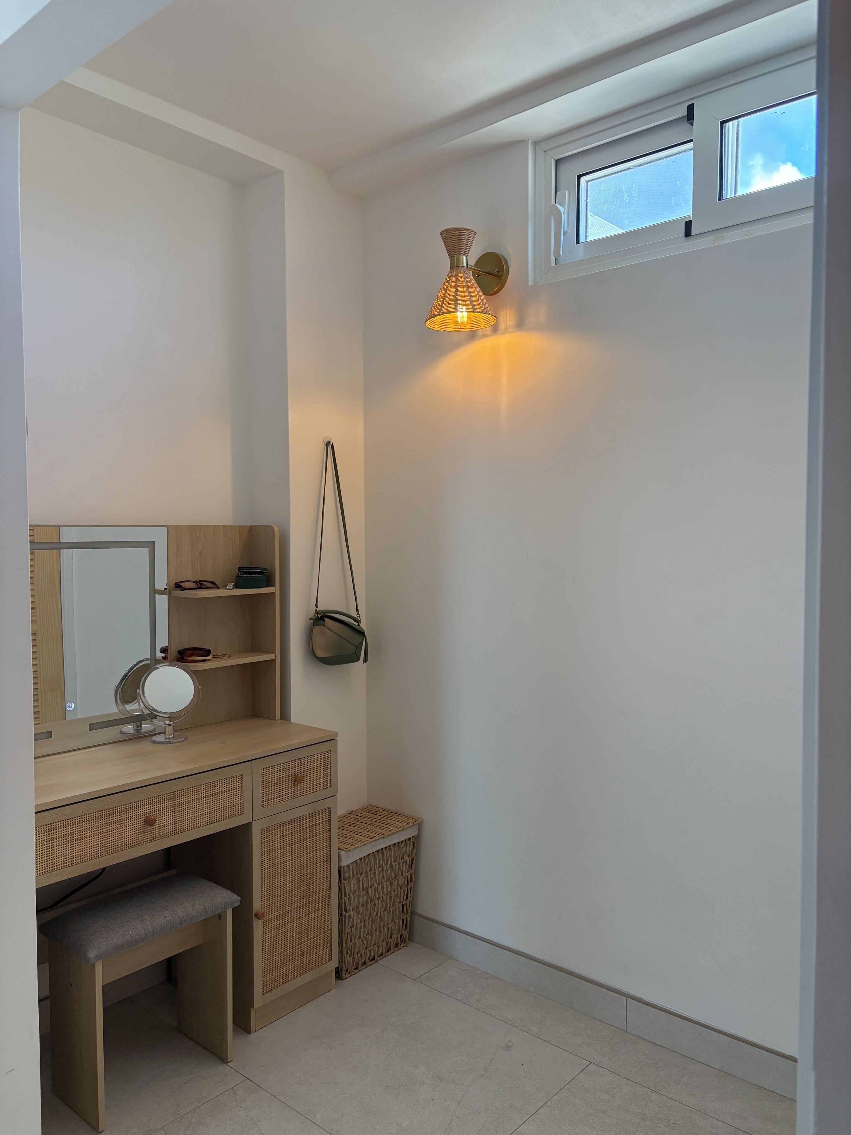 Une salle de bain avec un meuble-lavabo en bois, un miroir, une lampe suspendue, une petite fenêtre et un panier en osier.