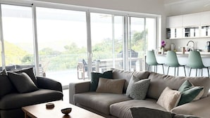 A modern living room with a large sofa set, a wooden coffee table, and a view of the outdoors through large windows. - Villa Kokomo · Breathtaking views 4BR Luxury Villa in Sugar Ridge w Private Pool (Jolly Harbour)