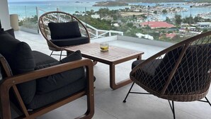 Un balcón con muebles de mimbre, una mesa de vidrio y vistas al mar y al pueblo.