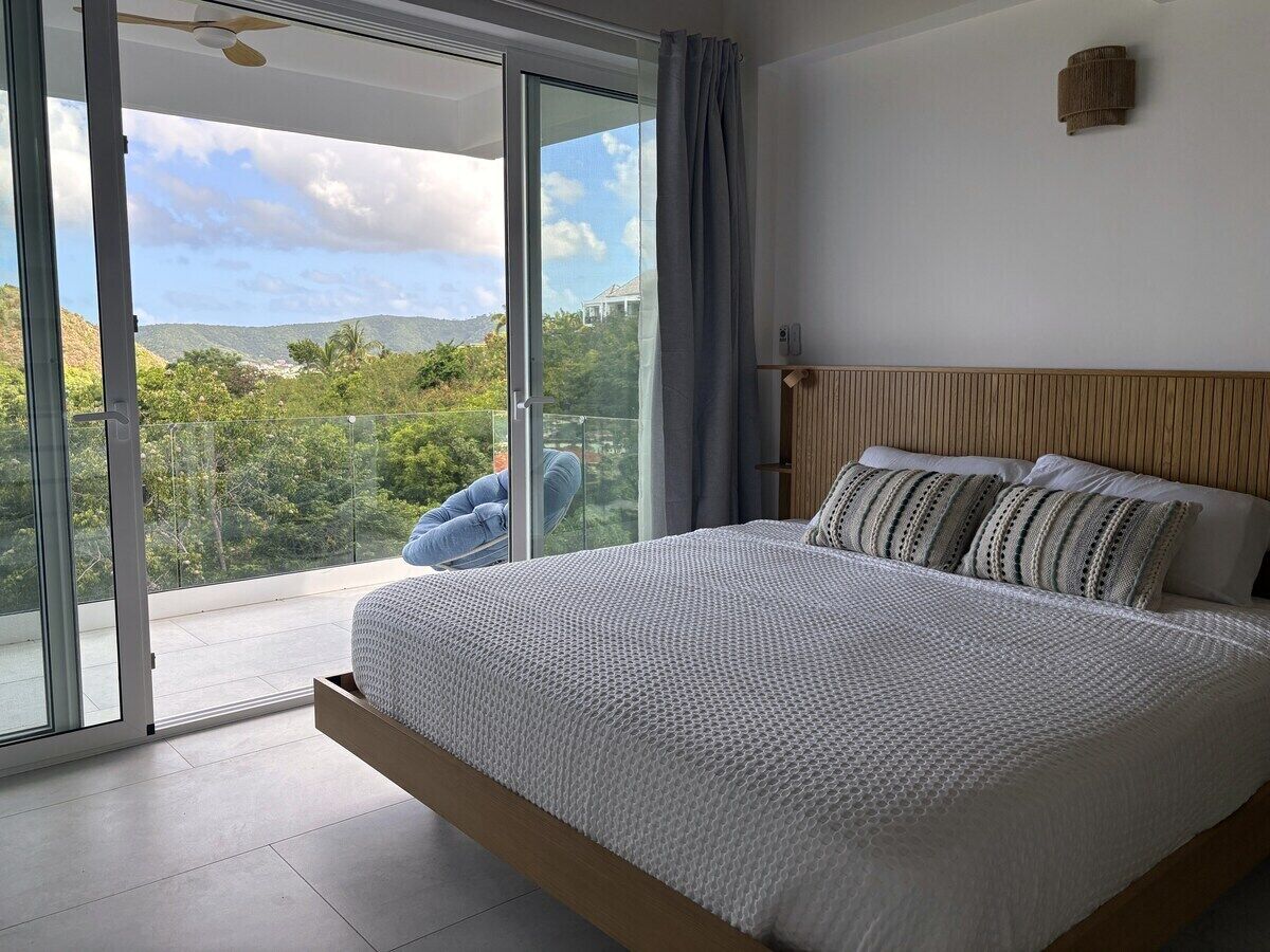 A bedroom with a large bed, a view through a sliding glass door, and a ceiling fan.