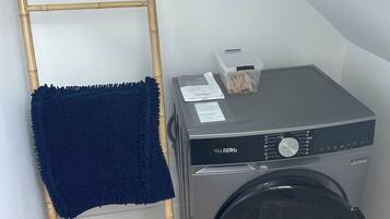 Een wasruimte met een wasmachine en droger, een houten ladder en een blauwe handdoek op de vloer.