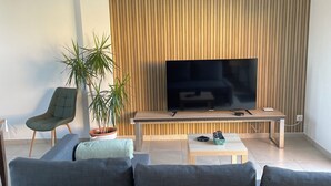 Un salon moderne avec un grand téléviseur à écran plat, un canapé, une table basse et deux plantes en pot.