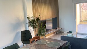 Un espace repas moderne avec une table en bois, des chaises recouvertes d’un tissu vert et une grande plante en pot.