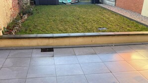 Une terrasse dallée, bordée de pierres, avec une pelouse verdoyante en arrière-plan.